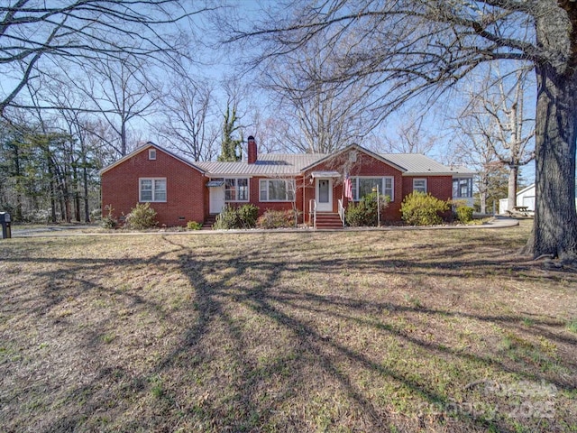 ranch-style house featuring a front yard, brick siding, metal roof, and a chimney