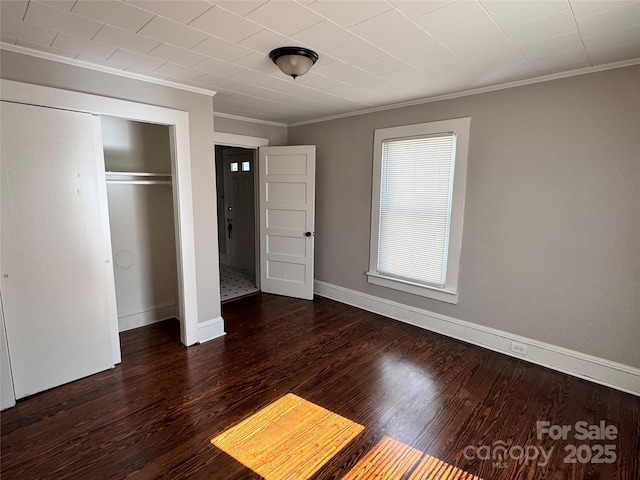 unfurnished bedroom featuring dark wood-type flooring, ornamental molding, and a closet