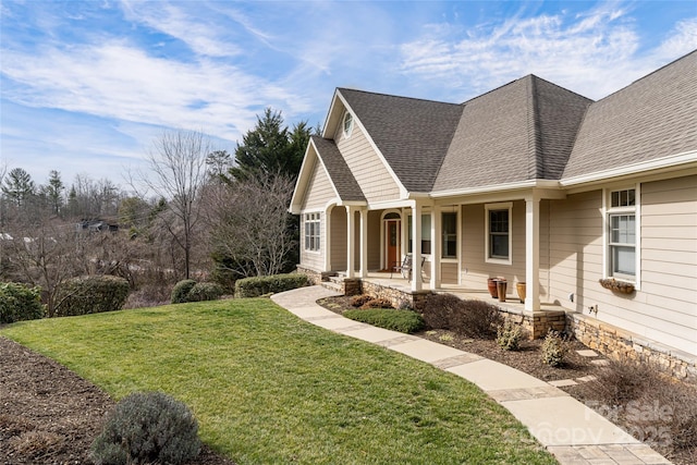 view of front of house featuring covered porch, a shingled roof, and a front lawn