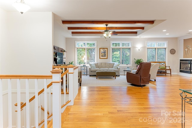 living area featuring a glass covered fireplace, beam ceiling, light wood-style flooring, and baseboards