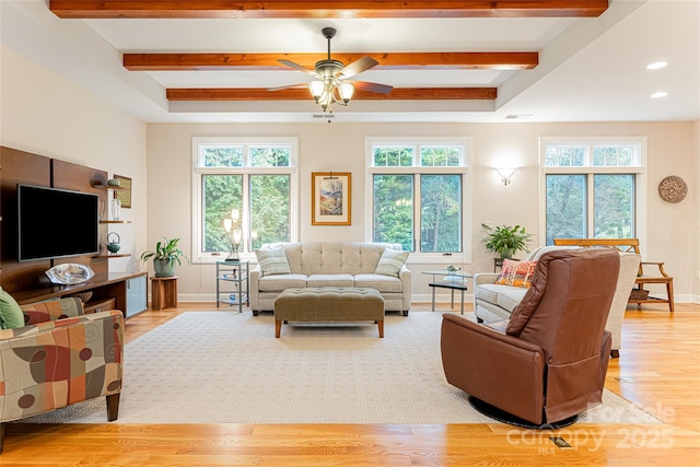 living area with beamed ceiling, light wood-type flooring, a ceiling fan, and baseboards