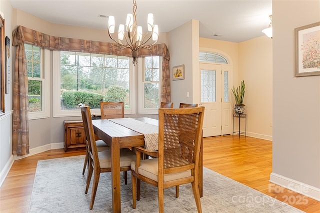 dining area with baseboards, visible vents, light wood finished floors, and an inviting chandelier