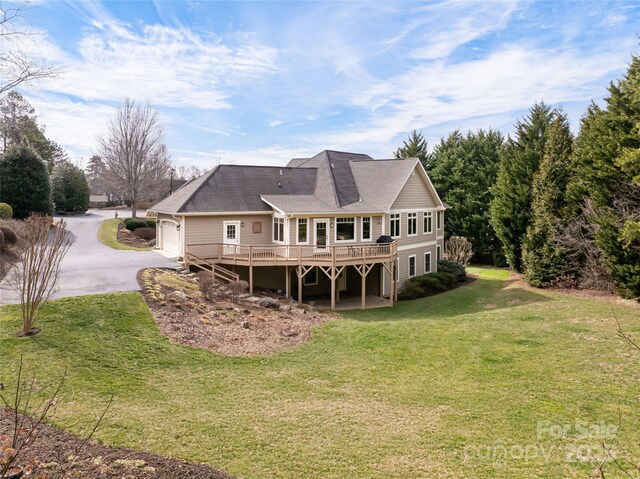 rear view of property with driveway, a deck, and a lawn