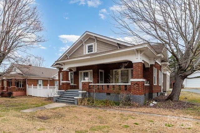 bungalow-style house featuring a porch, a front yard, crawl space, and brick siding