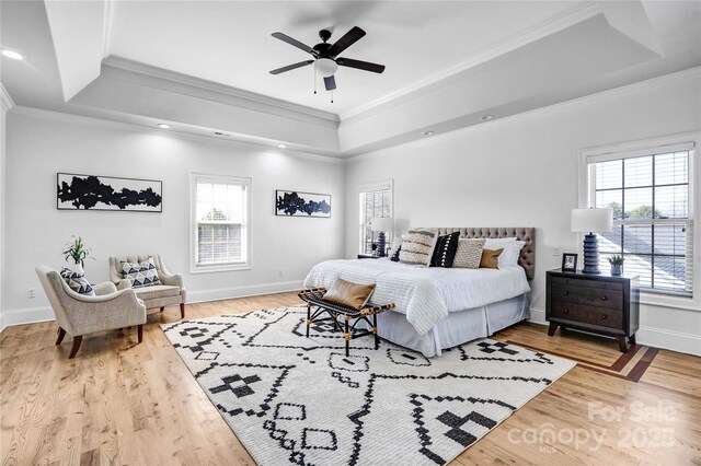 bedroom featuring light wood-style floors, baseboards, a raised ceiling, and crown molding