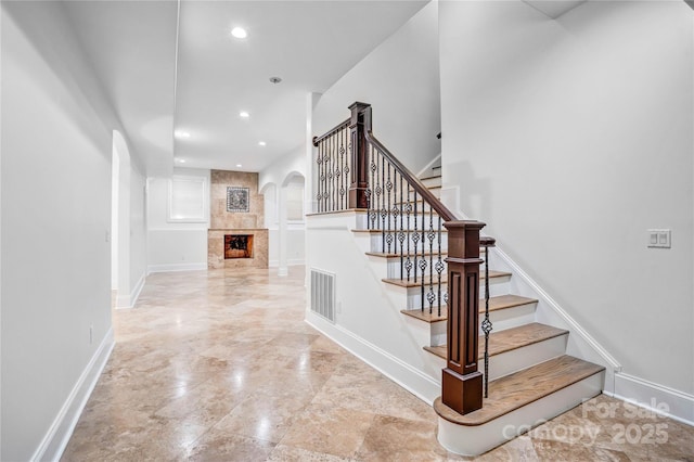 staircase featuring arched walkways, recessed lighting, a large fireplace, visible vents, and baseboards