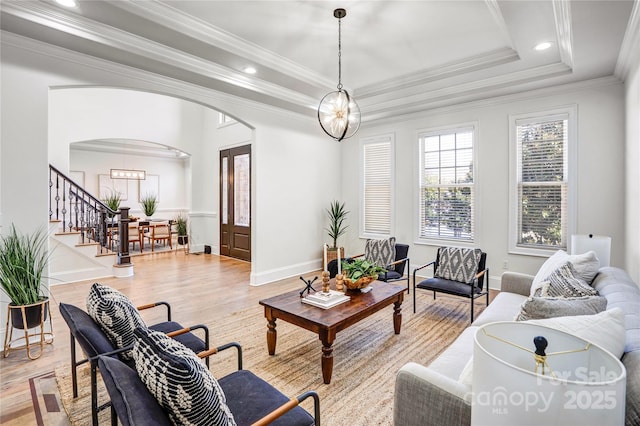 living room with light wood-style flooring, arched walkways, a raised ceiling, and stairway