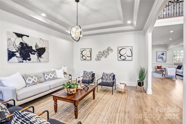 living area with arched walkways, recessed lighting, wood finished floors, ornamental molding, and a tray ceiling