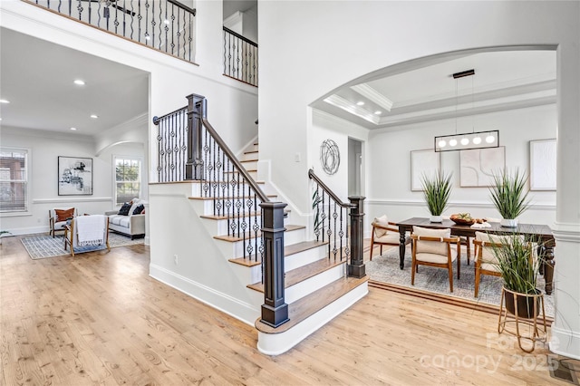 stairs with arched walkways, recessed lighting, wood finished floors, and crown molding