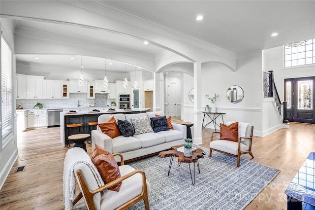 living area with light wood-type flooring, visible vents, arched walkways, and ornamental molding