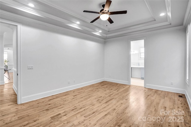 unfurnished room featuring light wood finished floors, baseboards, ceiling fan, a tray ceiling, and crown molding