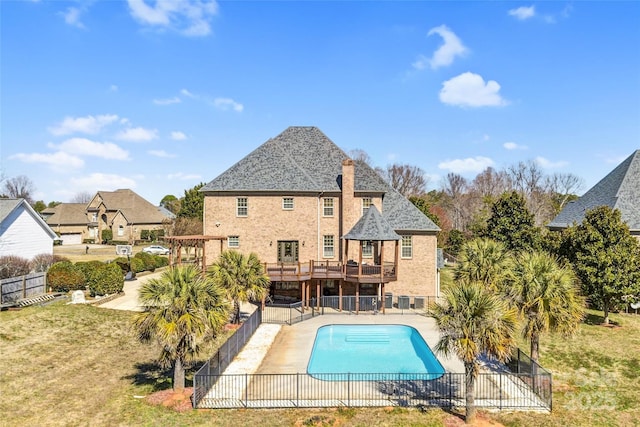 rear view of property featuring a deck, a patio, fence, a lawn, and a fenced in pool