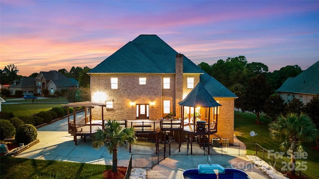 back of property at dusk featuring brick siding, a fenced in pool, a pergola, and a patio