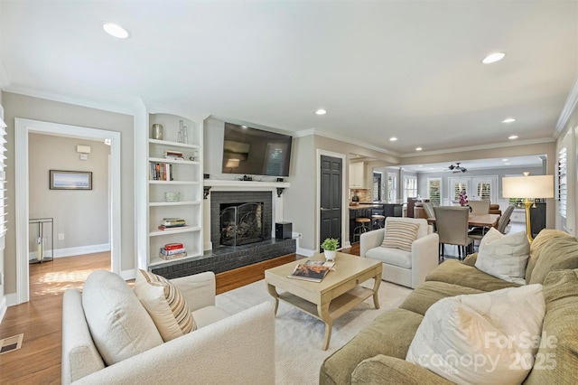 living room featuring light wood finished floors, baseboards, ornamental molding, a fireplace, and recessed lighting