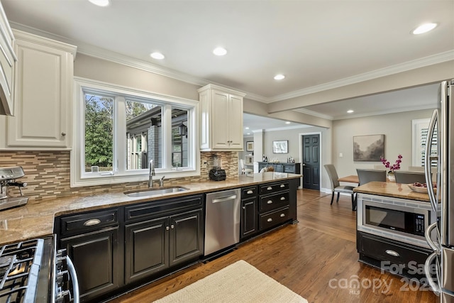 kitchen featuring light stone counters, dark wood-style flooring, a sink, appliances with stainless steel finishes, and dark cabinetry