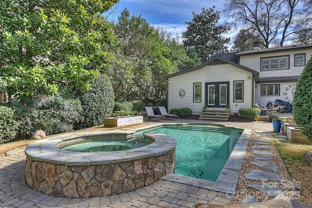 pool featuring entry steps, an in ground hot tub, and a patio