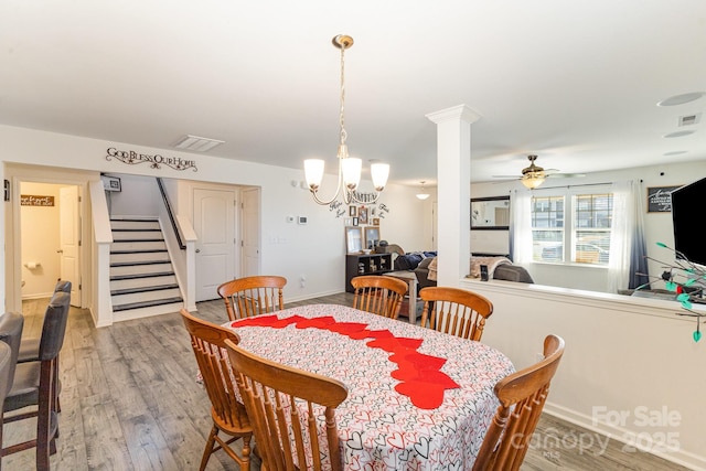 dining room featuring stairs, decorative columns, visible vents, wood finished floors, and ceiling fan with notable chandelier