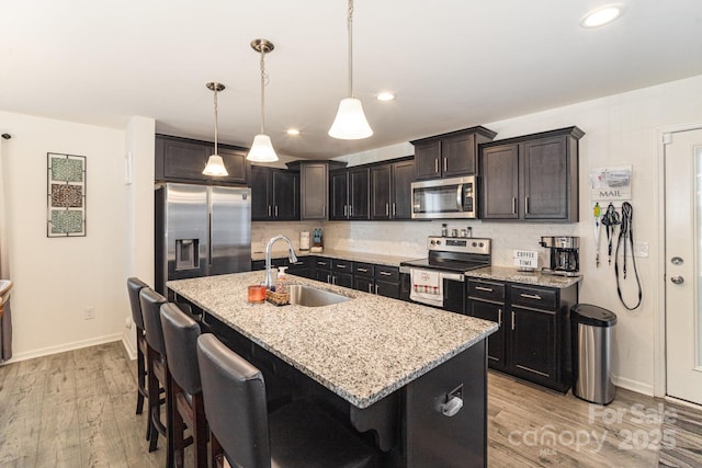 kitchen with a breakfast bar area, a sink, appliances with stainless steel finishes, an island with sink, and pendant lighting