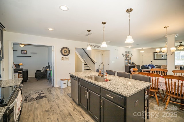 kitchen with light stone counters, pendant lighting, a center island with sink, appliances with stainless steel finishes, and a sink