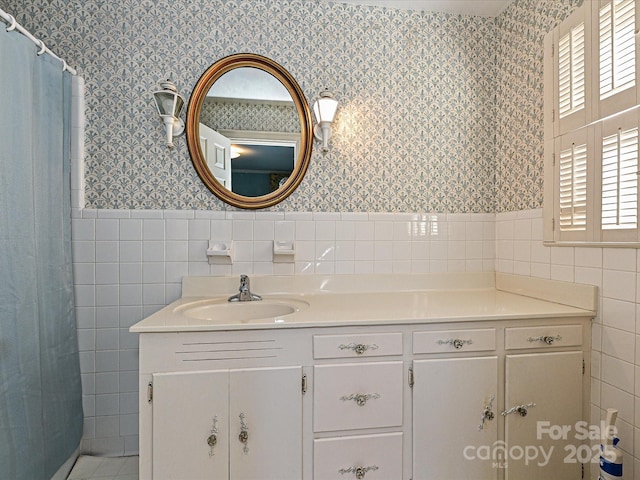 bathroom featuring wainscoting, vanity, tile walls, and wallpapered walls