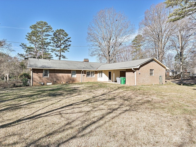 back of house featuring crawl space, brick siding, a lawn, and a chimney