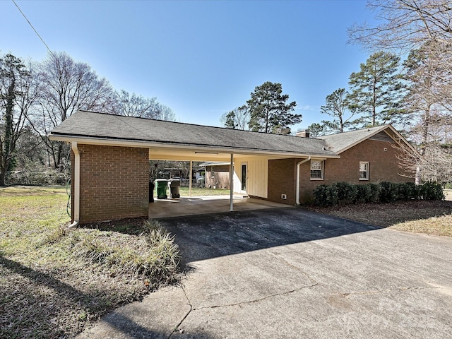 view of front facade with brick siding, a chimney, a shingled roof, a carport, and driveway