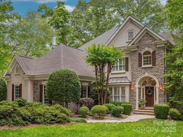 view of front of house with stucco siding, stone siding, a front yard, and a shingled roof