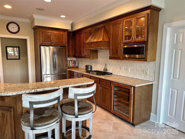 kitchen featuring beverage cooler, light stone counters, appliances with stainless steel finishes, decorative backsplash, and custom exhaust hood