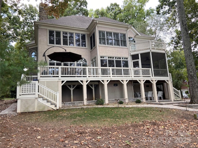 rear view of house featuring a wooden deck, stairs, stucco siding, a chimney, and a sunroom