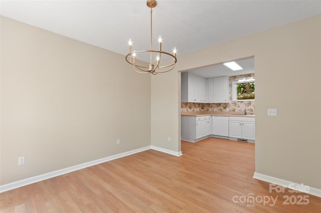 unfurnished dining area with a sink, baseboards, light wood finished floors, and a chandelier