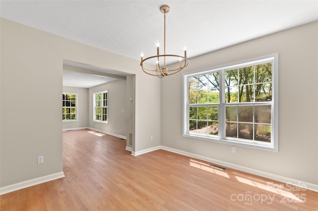 unfurnished room featuring baseboards, an inviting chandelier, and light wood-type flooring