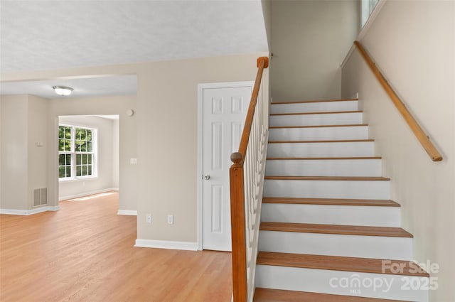 stairway featuring baseboards, wood finished floors, and visible vents