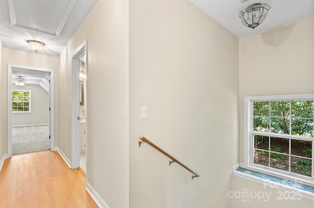 hallway featuring baseboards, an upstairs landing, light wood-style flooring, and attic access