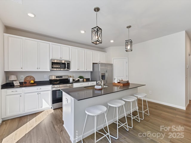 kitchen with stainless steel appliances, a sink, hanging light fixtures, an island with sink, and dark countertops