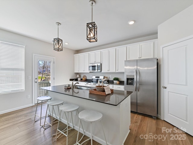 kitchen featuring dark countertops, a center island with sink, appliances with stainless steel finishes, and white cabinets