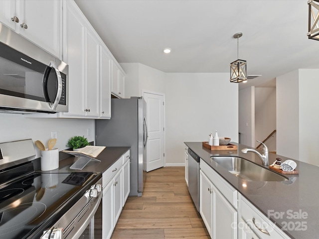 kitchen featuring decorative light fixtures, stainless steel appliances, white cabinetry, a sink, and light wood-type flooring