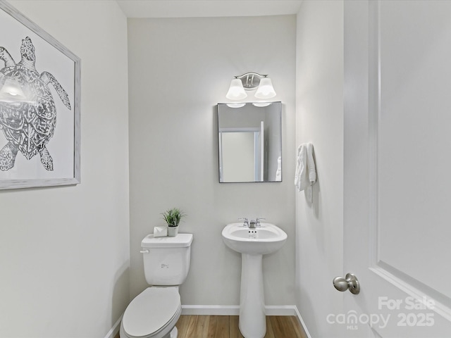 half bathroom with toilet, a sink, baseboards, and wood finished floors