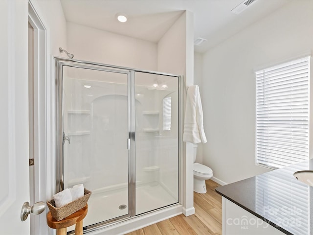 bathroom with visible vents, toilet, a stall shower, wood finished floors, and baseboards