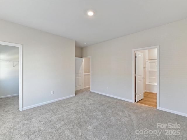 unfurnished bedroom with baseboards, a walk in closet, connected bathroom, and light colored carpet