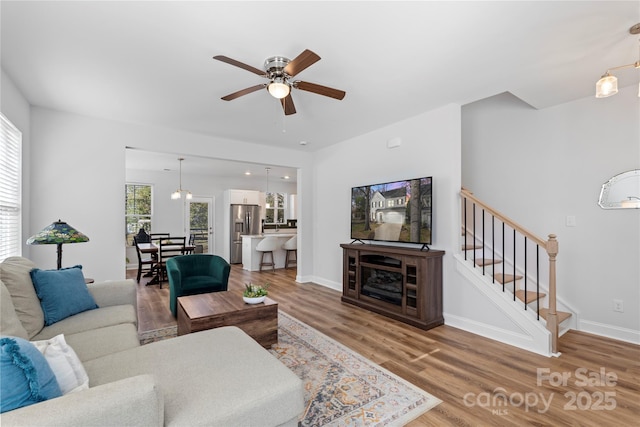 living room featuring a ceiling fan, stairway, baseboards, and wood finished floors