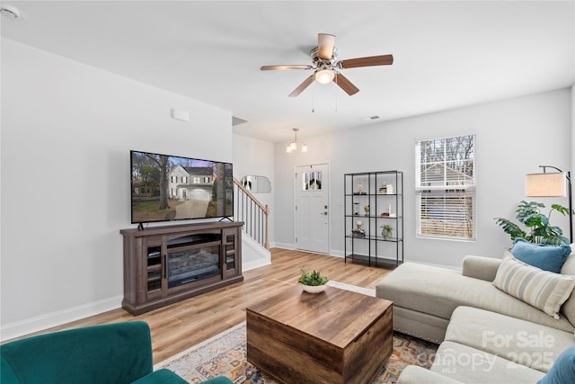 living room with stairs, visible vents, baseboards, and wood finished floors