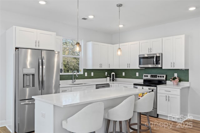 kitchen with appliances with stainless steel finishes, light countertops, a sink, and a center island