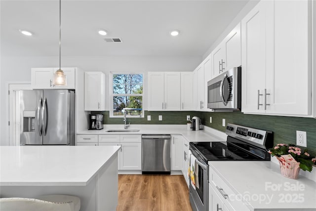 kitchen with appliances with stainless steel finishes, light countertops, decorative light fixtures, and a sink