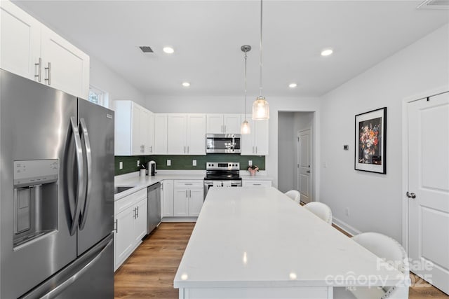 kitchen featuring appliances with stainless steel finishes, pendant lighting, white cabinetry, and a kitchen island