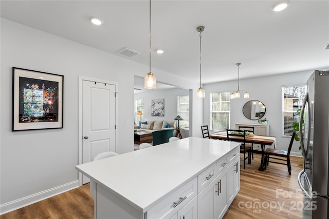 kitchen featuring white cabinets, a center island, freestanding refrigerator, light countertops, and pendant lighting