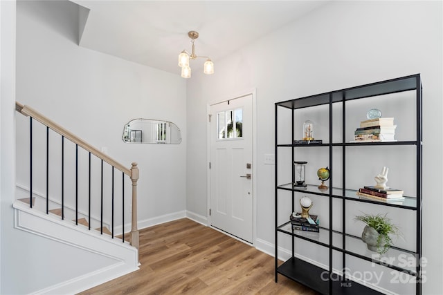 foyer entrance with wood finished floors, a notable chandelier, baseboards, and stairs