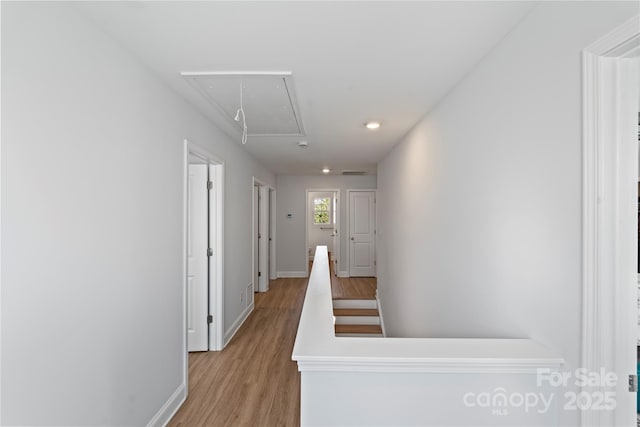 hallway with attic access, light wood-style floors, and baseboards