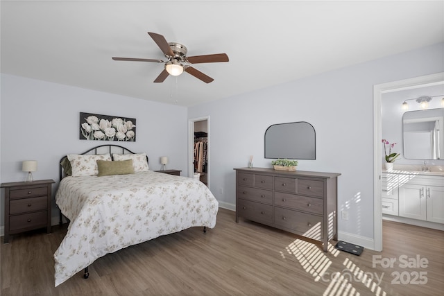 bedroom featuring a sink, baseboards, a walk in closet, and wood finished floors