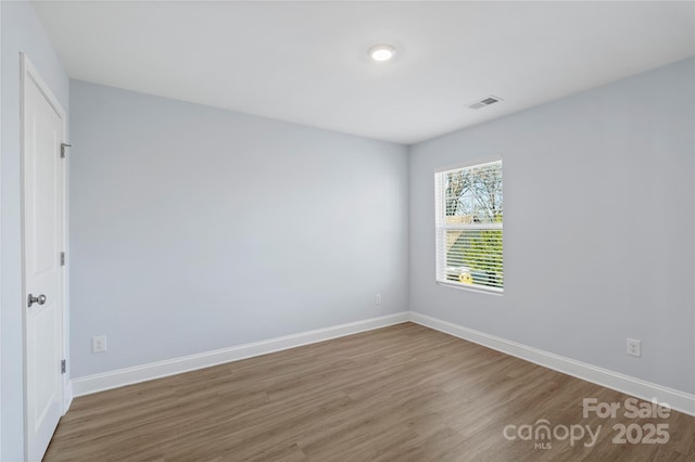 empty room with baseboards, visible vents, and wood finished floors