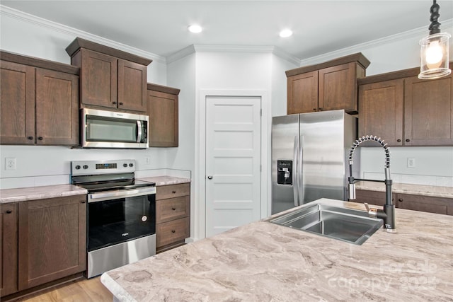 kitchen with hanging light fixtures, appliances with stainless steel finishes, light stone countertops, and ornamental molding